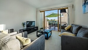 A modern living room with a sofa, coffee table, TV, and a balcony with an umbrella.
