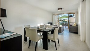 A modern dining area with a black table and white chairs, a small side table with a lamp, and a view of the outdoor patio through large glass doors.