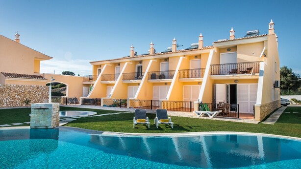 A hotel with a swimming pool, multiple balconies, and a stone wall.