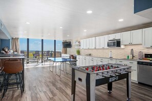 A modern kitchen with a foosball table, a dining area with chairs, and a view of the sea.