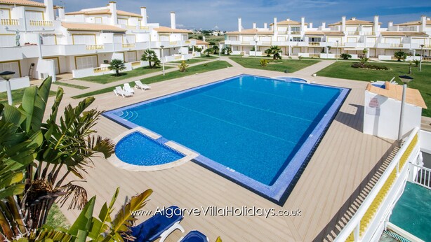A large swimming pool surrounded by a deck, with white buildings in the background. - Apartment AG - O Monte 3 bedroom apt with large pool (Albufeira)