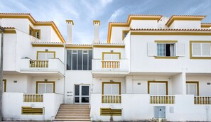 Un edificio blanco con detalles amarillos, varios balcones y una entrada central con escalones.