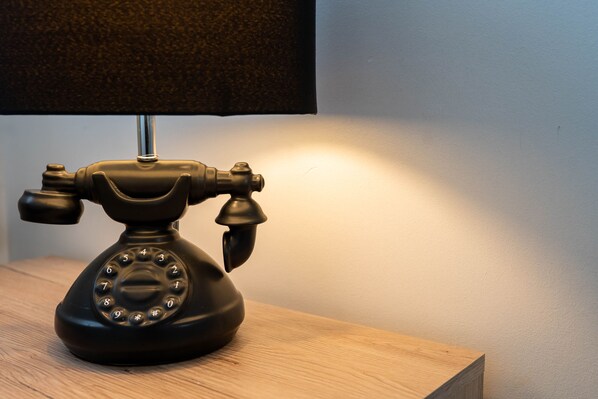 A black rotary telephone on a wooden table with a lamp casting a warm light. - Queen Anne's Home (Great Yarmouth)