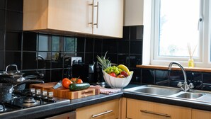 A modern kitchen with black tiles, wooden cabinets, a gas stove, a sink, and a fruit bowl on the counter. - Queen Anne's Home (Great Yarmouth)