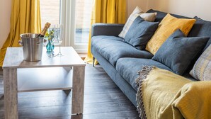 A living room with a grey sofa, yellow curtains, a wooden coffee table, and a metal bucket with a bottle and glasses. - Queen Anne's Home (Great Yarmouth)