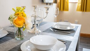 A dining table set with white plates, bowls, and cutlery, a vase with yellow flowers, and a wine glass. - Queen Anne's Home (Great Yarmouth)