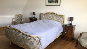 A bedroom with a large bed, a chair, a nightstand, and a framed picture on the wall. - Gite Alcove in a farmhouse beach and coastal path on foot (Névez)