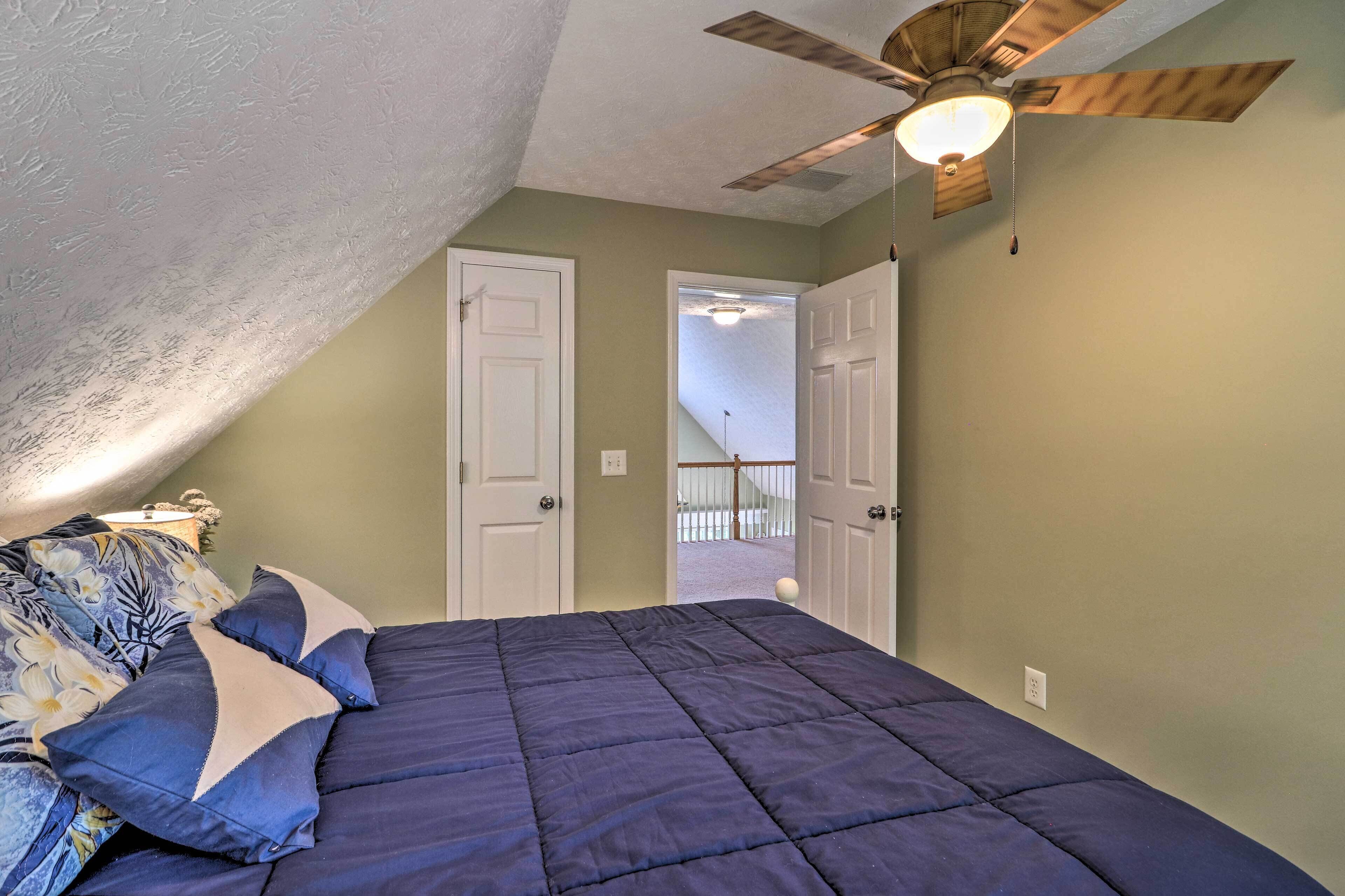A bedroom with a dark blue bed, a ceiling fan, and a door leading to a balcony.