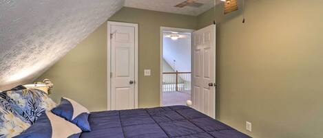 A bedroom with a dark blue bed, a ceiling fan, and a door leading to a balcony.