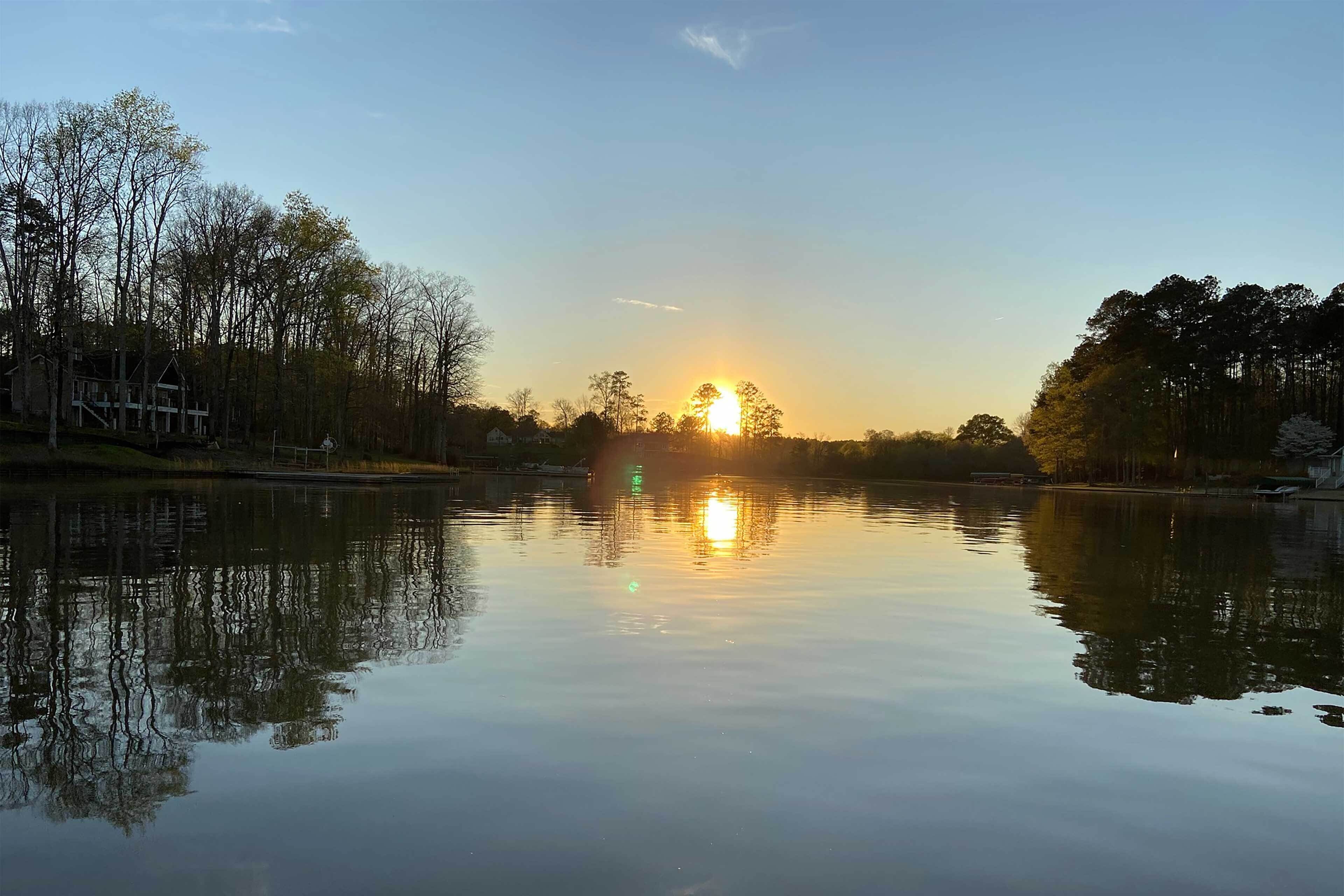 A calm lake with a sunset reflection, surrounded by trees and a house.