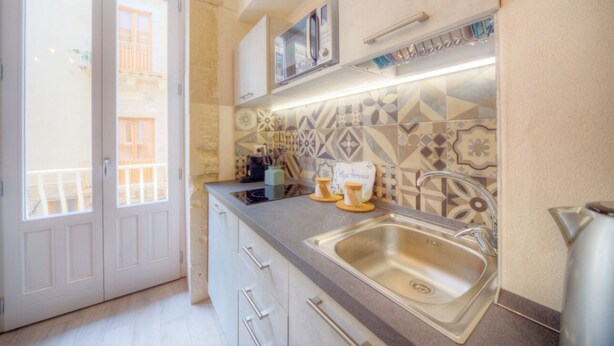 A kitchen with a stainless steel sink, a tiled backsplash, and a window overlooking a balcony. - GuestHost - Ortigia Promenade - Bright and Comfortable Apartment (Siracusa)