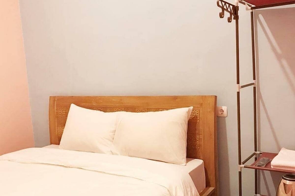 Un lit simple avec une tête de lit en bois, une étagère en métal et une petite table avec une bouilloire.
