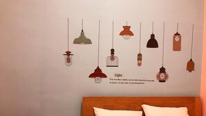 A bedroom with a bed, pillows, a nightstand, a kettle, and a wall with hanging light fixtures and a motivational quote. - Roomz Budget (Semarang)