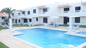 A swimming pool with lounge chairs and umbrellas, surrounded by a white building with balconies. - Roca Belmonte Apartamentos (Albufeira)