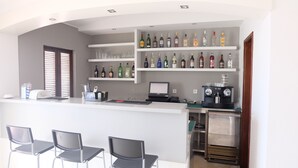 A bar area with a counter, multiple shelves of liquor bottles, a coffee machine, and three chairs. - Roca Belmonte Apartamentos (Albufeira)