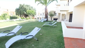 A courtyard with sun loungers, a palm tree, and a building with balconies. - Roca Belmonte Apartamentos (Albufeira)