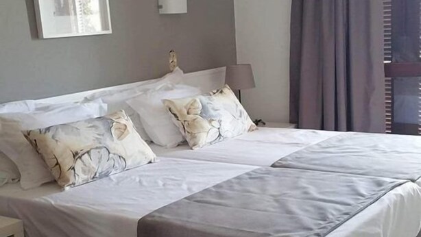A bedroom with a large bed, a bedside table, a lamp, a framed picture on the wall, and a window with curtains. - Roca Belmonte Apartamentos (Albufeira)