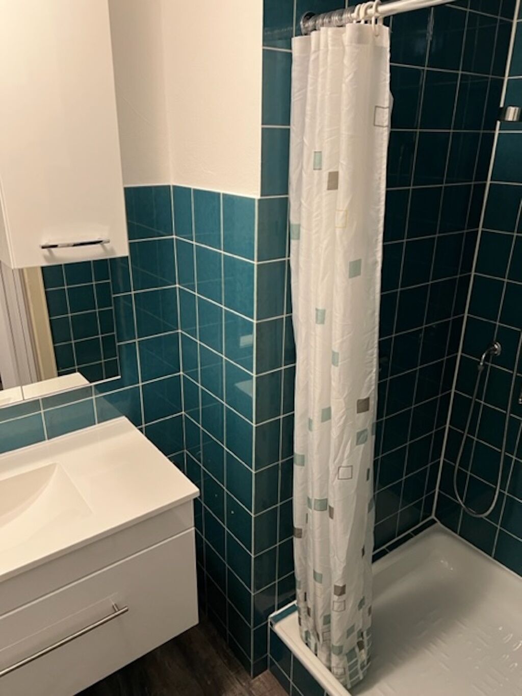 A bathroom with a white sink, a mirror, and a shower with a white curtain.