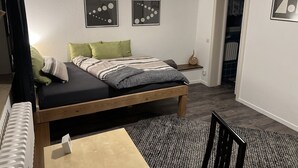 Quarto com cama, almofadas, mesa de cabeceira, tapete e duas obras de arte na parede.