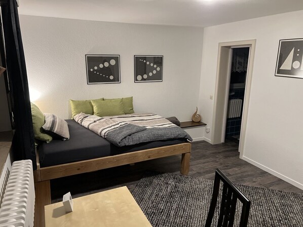 A bedroom with a bed, pillows, a bedside table, a rug, and two wall art pieces.