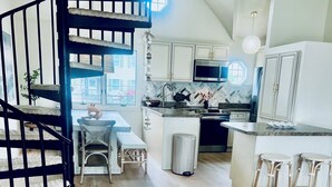 Une cuisine moderne avec un îlot central, un coin repas comprenant une table et des chaises, un fauteuil bleu et un escalier en colimaçon.