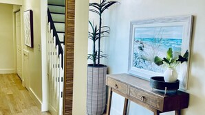 Un couloir doté d’un plancher en bois, d’un escalier, d’une console sur laquelle sont posés un vase et un tableau encadré, ainsi qu’un grand miroir.