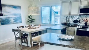 Une cuisine moderne dotée d’un grand îlot central, de planchers en bois et d’un coin repas avec des tabourets en osier.