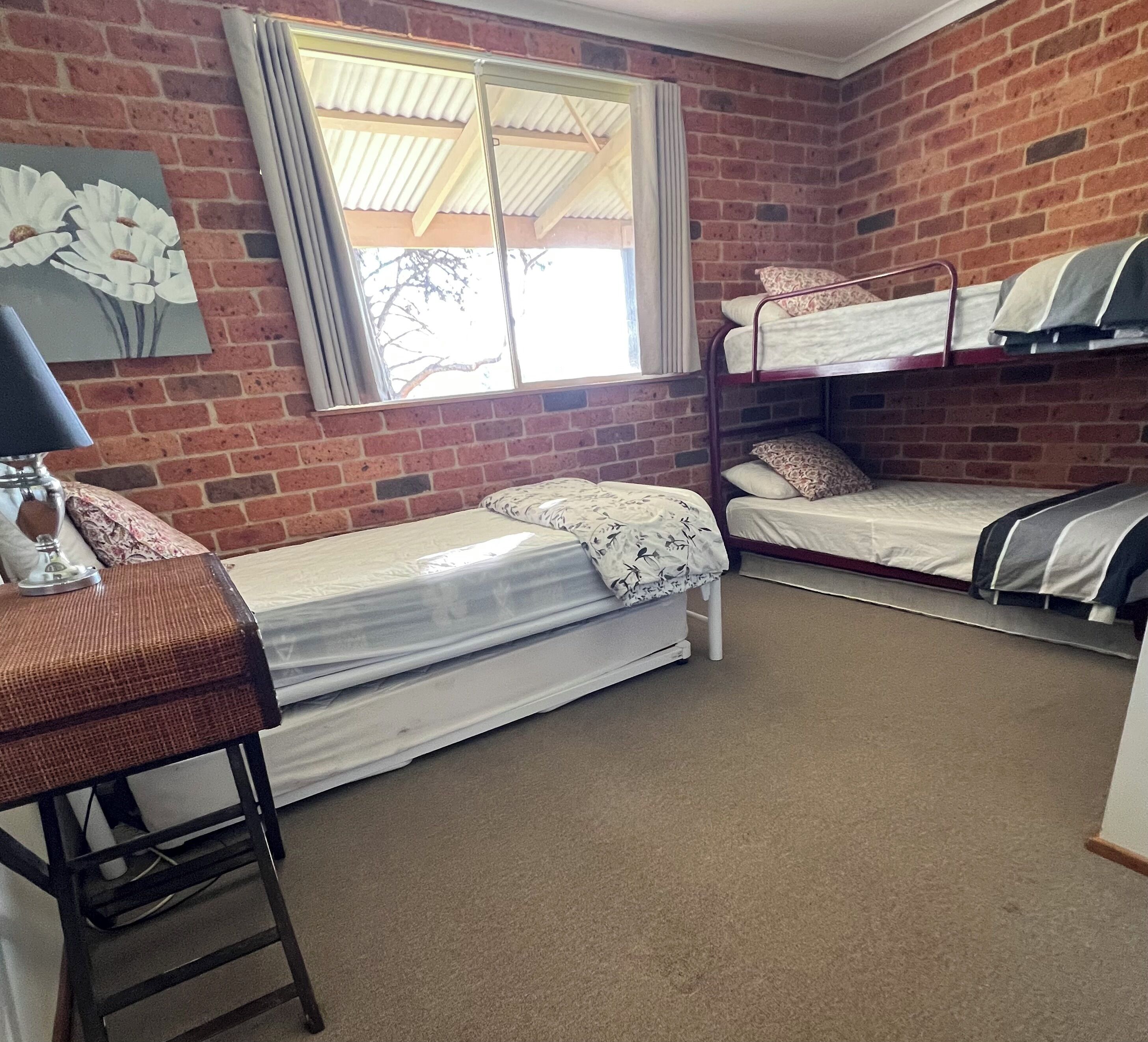 A dormitory room with two bunk beds, a desk, and a window with curtains.