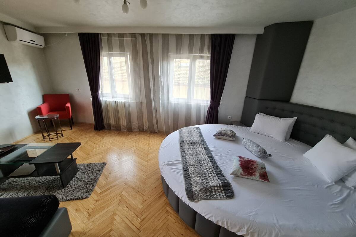 A hotel room with a large bed, a red chair, a small table, and a TV.