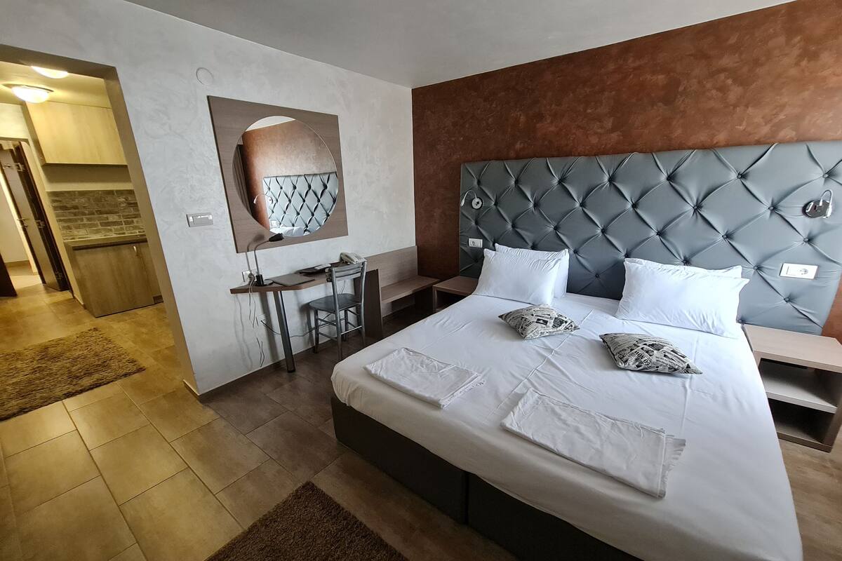 A modern hotel room with a large bed, a desk, and a mirror.