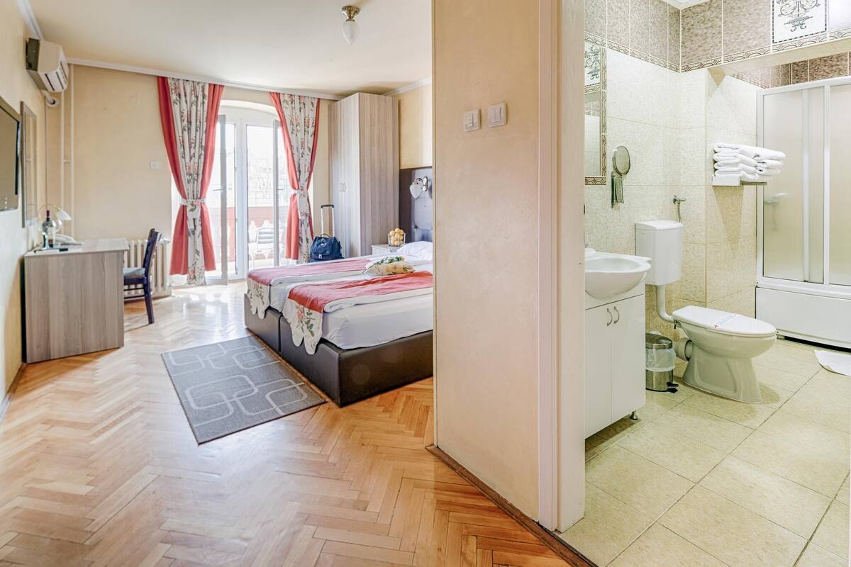 A hotel room with a bed, a desk, a chair, a bathroom with a toilet, sink, and mirror.