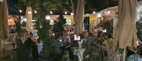 An outdoor dining area with tables and chairs, surrounded by potted plants and umbrellas.