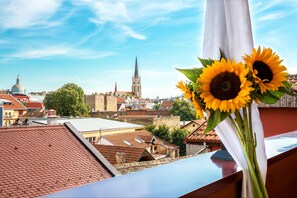 A cityscape with a prominent church spire, a tiled roof, and a bouquet of sunflowers. - Hotel Fontana (Novi Sad)