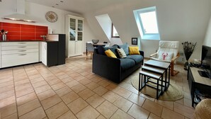 A modern loft apartment with a kitchen, dining area, and living room. It features a sloped ceiling, a skylight, and a large window.
