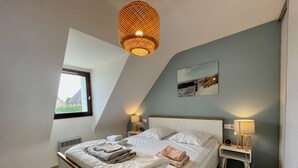 A bedroom with a sloped ceiling, a bed with white linens, two bedside lamps, a window, and a wall-mounted painting.