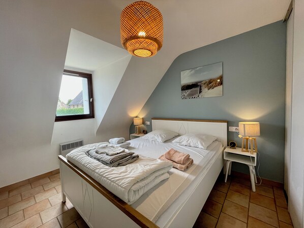 A bedroom with a sloped ceiling, a bed with white linens, two bedside lamps, a window, and a wall-mounted painting.