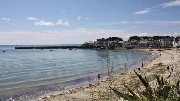 A beach with a pier, buildings in the background, and clear skies.