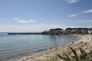 A beach with a pier, buildings in the background, and clear skies.