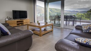 A modern living room with a sofa, a coffee table, and a TV. There's a balcony with a view of the hills. - A Mont Nos Hôtes view of the Ventoux (Mollans-sur-Ouvèze)