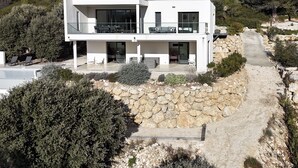 A modern two-story house with a stone retaining wall, a balcony with outdoor seating, and a pathway leading to the entrance. - A Mont Nos Hôtes view of the Ventoux (Mollans-sur-Ouvèze)