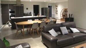 A modern living room with a leather sofa, dining table, and chairs. A kitchen with appliances and a small island is visible in the background. - A Mont Nos Hôtes view of the Ventoux (Mollans-sur-Ouvèze)