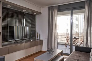 A modern living room with a flat-screen TV, a coffee table, and a sofa. There is a balcony with outdoor furniture visible through the window. - Contemporary and comfortable apartment next to the Acropolis Museum (Athens)