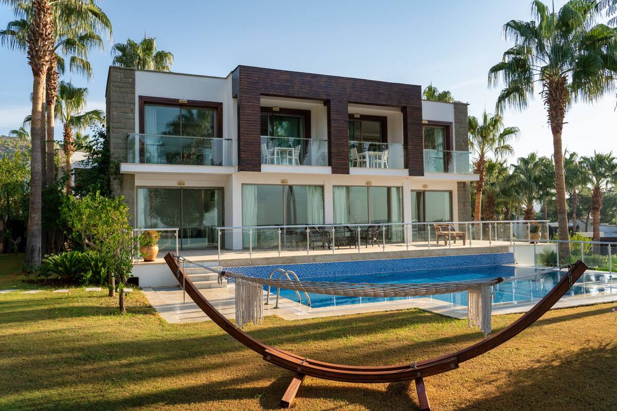 A modern two-story house with a swimming pool, palm trees, and a hammock.