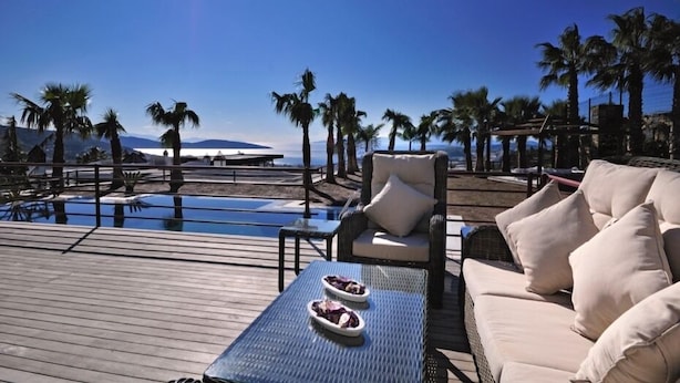 A poolside area with a lounge chair, a small table with a plate of food, and a view of palm trees and mountains in the background. - Hillstone Bodrum Hotel & Spa (Bodrum)