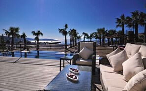 Un espace aménagé au bord de la piscine, avec un fauteuil de relaxation, une petite table sur laquelle se trouve une assiette de nourriture, et en arrière-plan, une vue sur des palmiers et des montagnes.