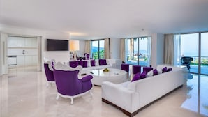 A modern living room with a white sofa, purple armchairs, and a coffee table. There is a TV mounted on the wall, and large windows offering a view of the ocean. - Hillstone Bodrum Hotel & Spa (Bodrum)