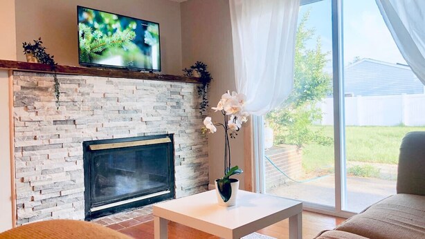 Un salón con chimenea de piedra, un televisor de pantalla plana montado encima y una mesa de centro blanca, además de un sofá.