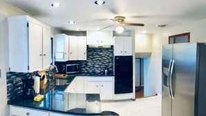 Una cocina moderna con armarios blancos, encimera negra, refrigerador de acero inoxidable y ventilador de techo.