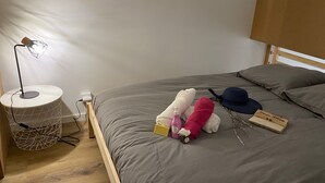 Un llit ben fet amb llençols grisos, una làmpada de nit i objectes personals com un barret, una ampolla i una caixa damunt del llit.