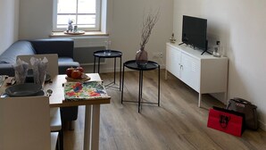 Un saló modern amb un sofà, taula de menjador i televisió. Hi ha tres llums penjants, una finestra i un armari.